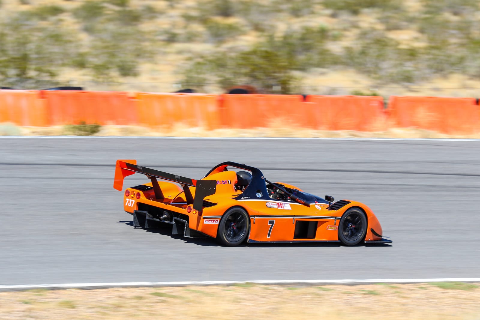 An orange FastLane Radical SR3 sports racer at speed on track at Buttonwillow Raceway.