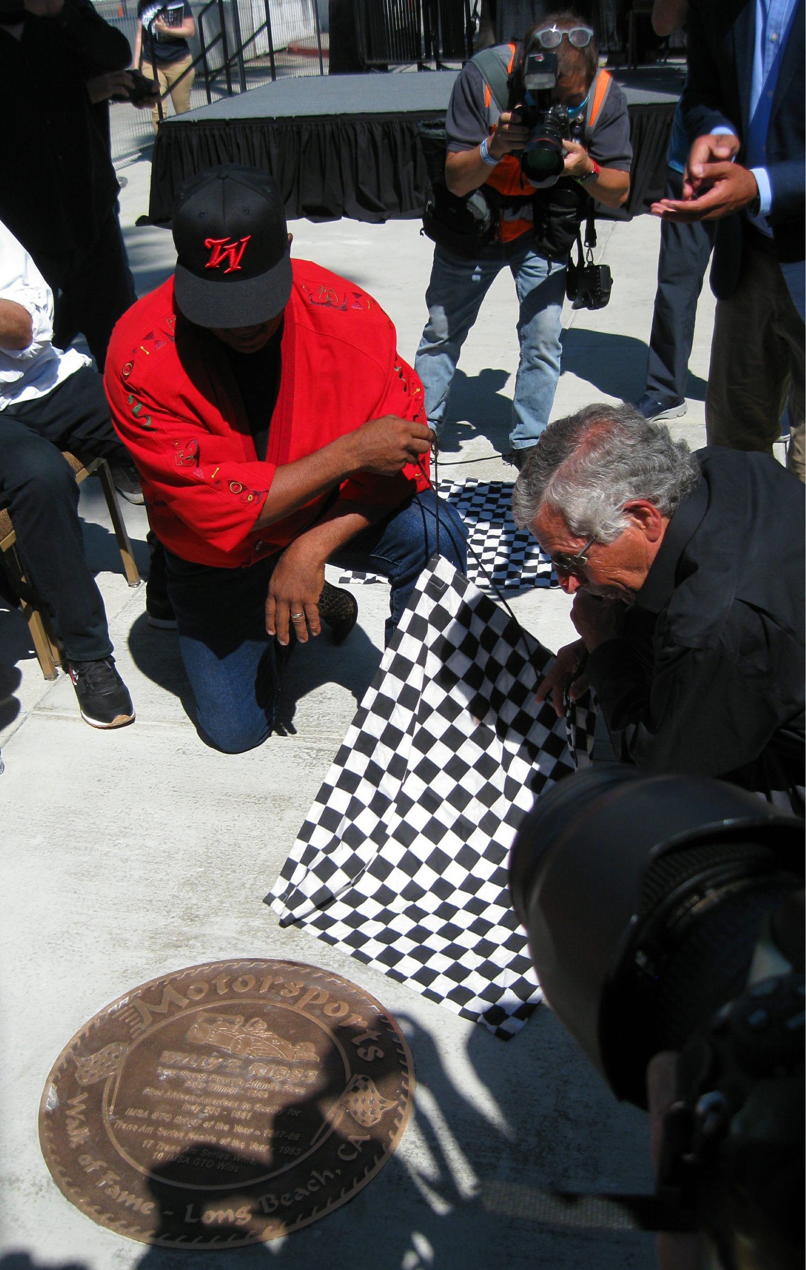 Willy T. Ribbs and Jim Michaelian (president and CEO of the Grand Prix Association of Long Beach) remove the checkered flag to uncover the Long Beach Motorsports Walk of Fame plaque for Ribbs.
